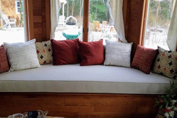 A window seat with a white cushion and red and white pillows adorning it.